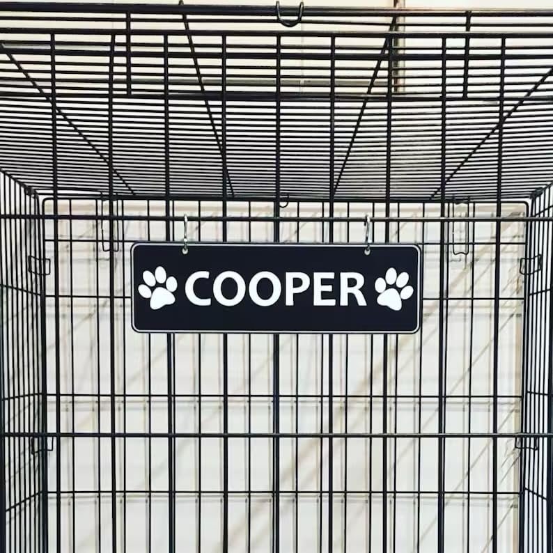 Dog crate with a sign that says "Cooper" and paw prints